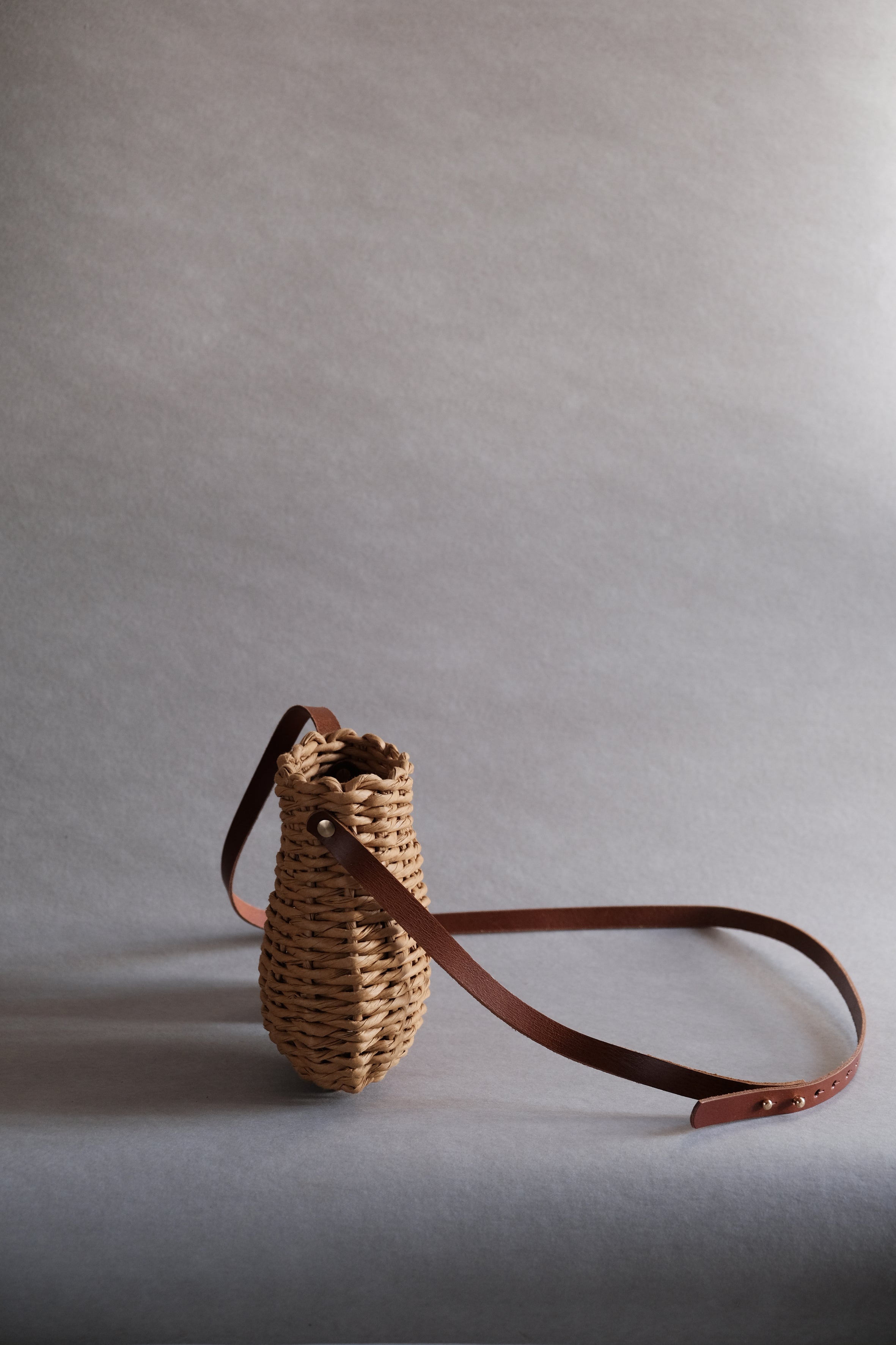 フランス製紙撚り糸をデザイナーが手編みしたCOCOON CROSSOVER(コクーン クロスオーバー)。繭のような丸いフォルムを一本のレザーストラップが引き立てる、オーストリア製ハンドメイドショルダーバッグ。