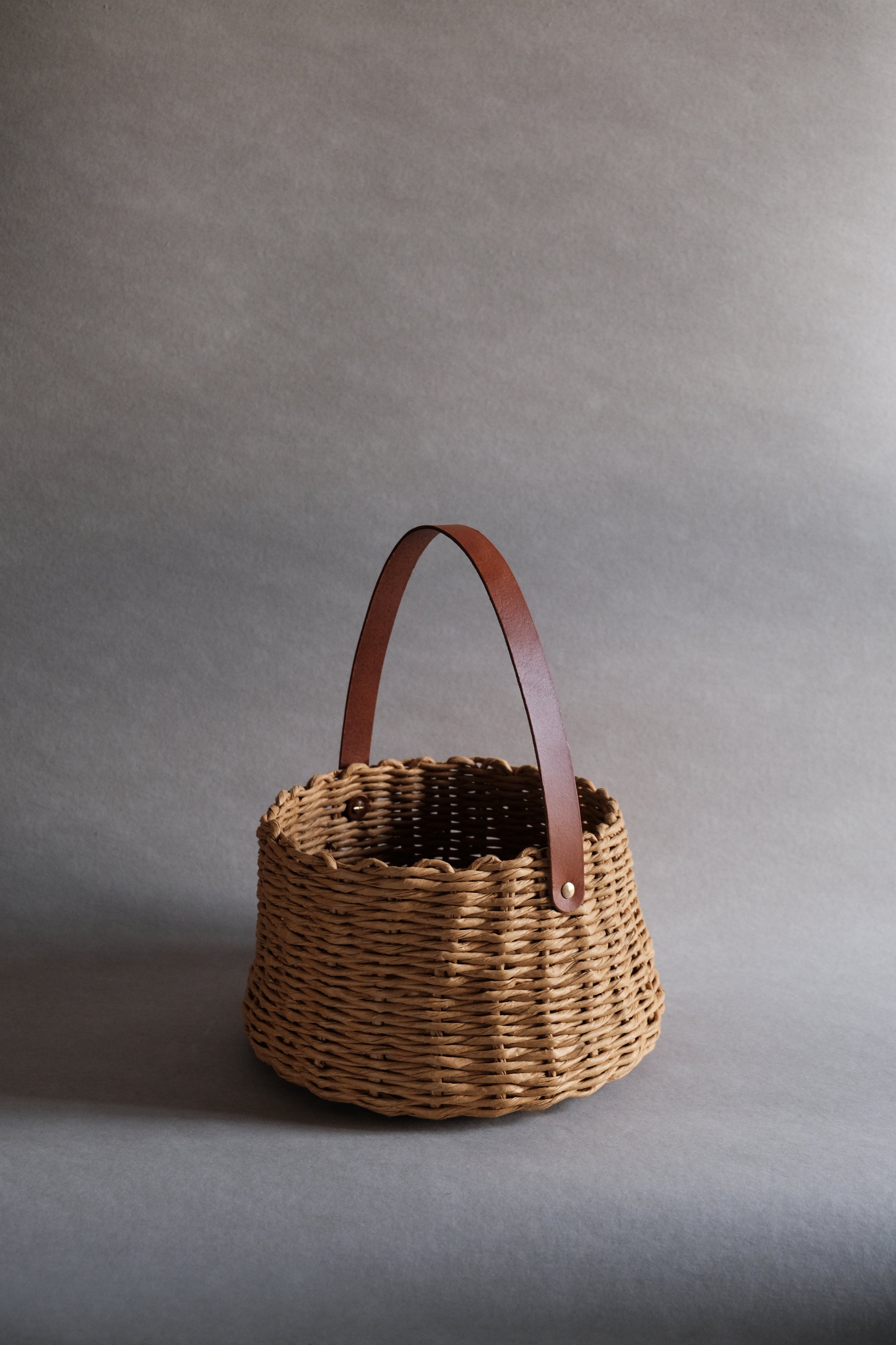 フランス製紙撚り糸をデザイナーが手編みしたCOCOON BASKET（コクーン バスケット）。丸みのある繭のようなフォルムと、真鍮金具で固定されたレザーハンドルが美しい、オーストリア製ハンドメイドのカゴバッグ。